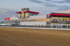 La tribune du Century Mile avec ses enseignes CASINO et RACING, vue de l'autre côté de la piste en terre battue, au crépuscule