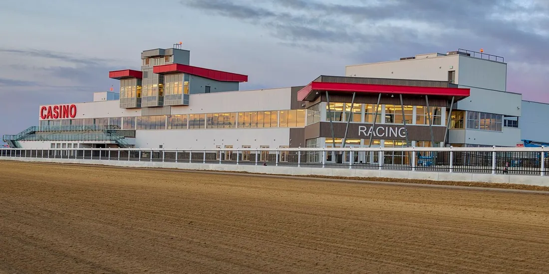La tribune du Century Mile avec ses enseignes CASINO et RACING, vue de l'autre côté de la piste en terre battue, au crépuscule